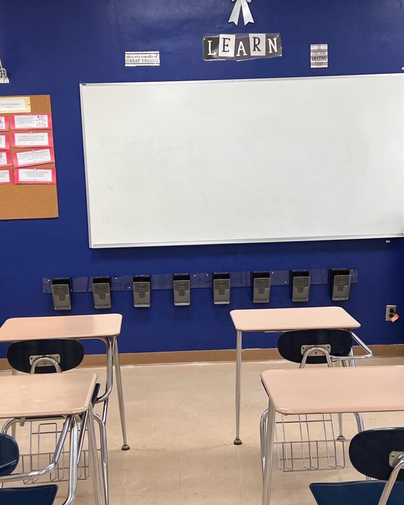A classroom with desks and chairs in front of a white board.