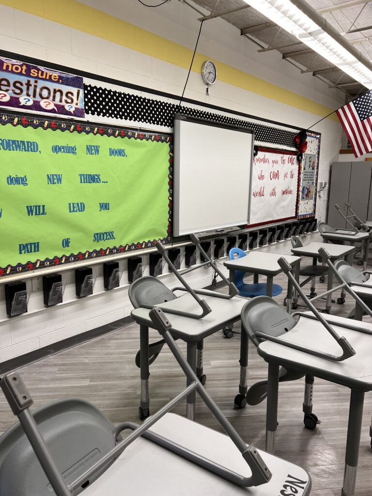 A classroom with desks and chairs in front of a whiteboard.